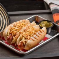 2 Mini Perro Caliente · Mini hot dogs topped with potato chips and pink sauce.