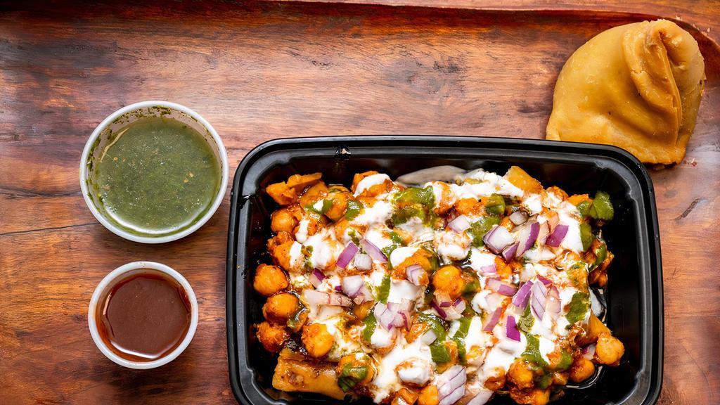 Samosa Chaat · Crispy samosa served with chickpeas masala, yoghurt, tamarind date, cool mind and coriander chutney. Topped with tomatoes, onions, cilantro, chickpea noodles and spice blend.