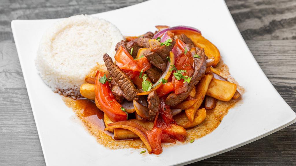 Peruvian Lomo Salteado · Chunks of sirloin, red onion, tomato slices, served over french fries and accompanied with white rice.