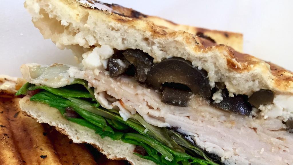 Greek Panini · Turkey breast, crumbled feta cheese, black olives, greens, balsamic and Greek seasonings on flatbread.