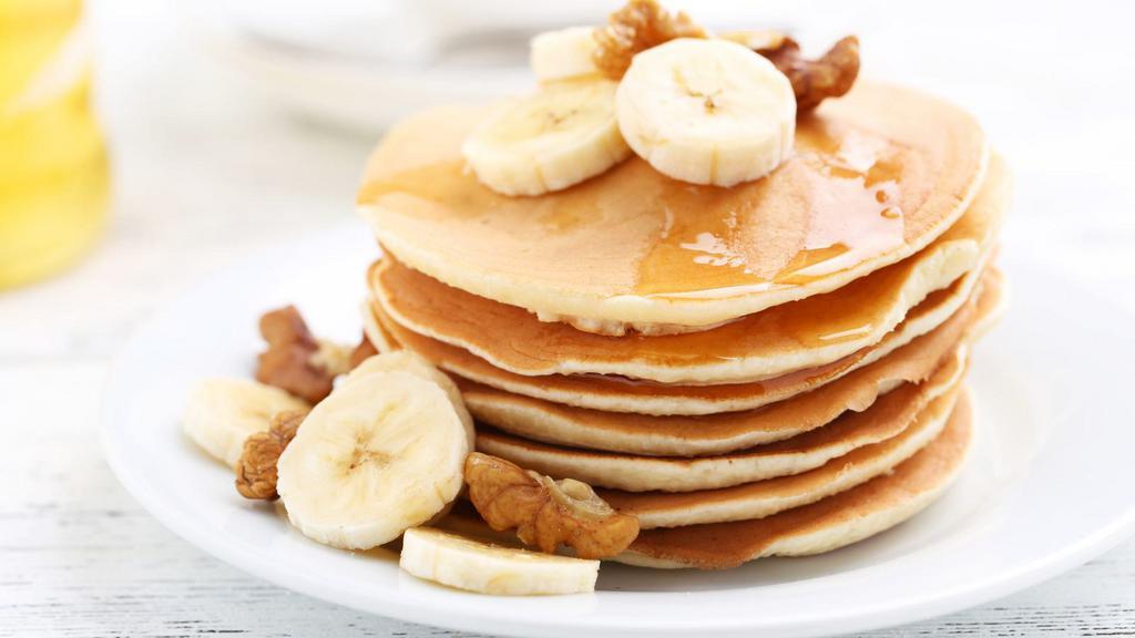 Banana Pancakes · Fresh pancakes topped with bananas and served with a side of syrup and butter.