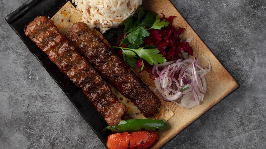 Lamb Adana Kebab · Hand chopped lamb seasoned with spicy red bell peppers, then char-grilled. Served with rice, peppers and onions, lettuce and a side of red and white sauces.