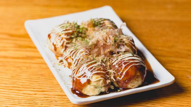 Takoyaki · Six pieces. Grilled octopus balls that are crispy on the outside, soft and doughy on the inside. Slathered with takoyaki sauce, sprinkled with green laver (aonori), and garnished with dried bonito flakes.