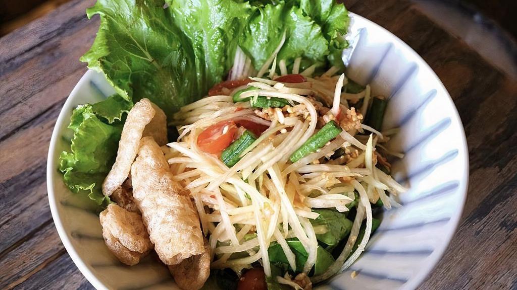 Papaya Salad · Gluten-free. Spicy. Shredded green papaya, long beans, tomatoes, and peanuts with Thai chili-lime dressing and topped with crispy pork rinds.