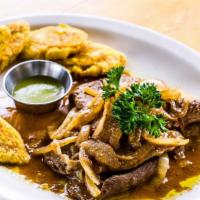 Bistec Encebollado · Marinated palomilla sirloin steak sautéed with red wine and onions, served with tostones.