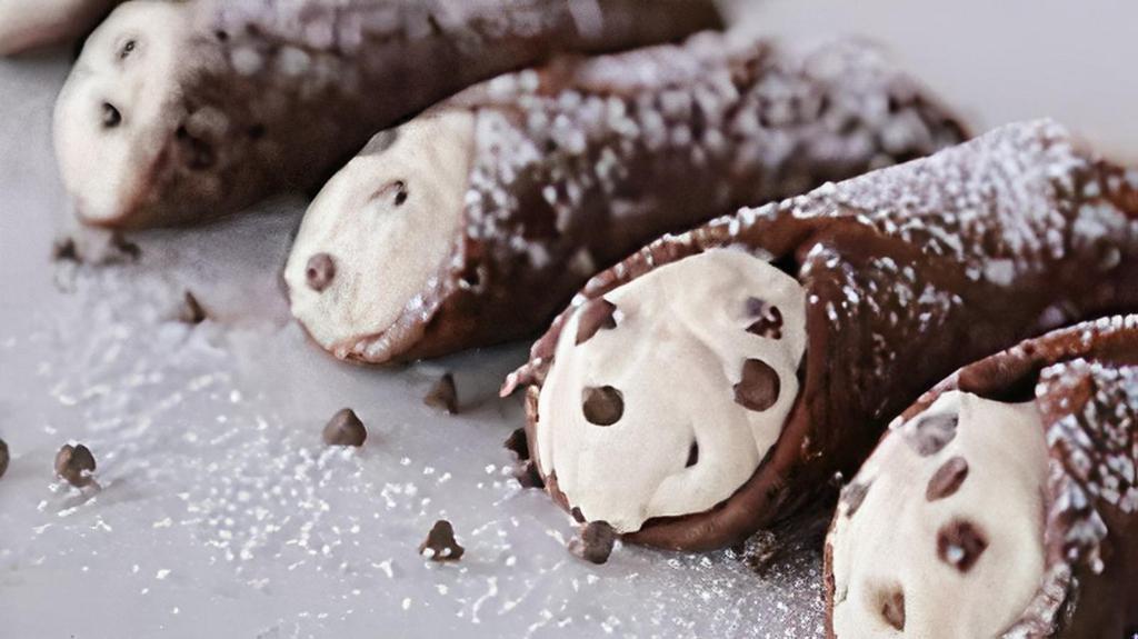 Chocolate-Dipped Cannoli · Crispy Italian shell dipped in chocolate filled with sweet ricotta cheese, chocolate chips, and a hint of cinnamon, dusted with powdered sugar.