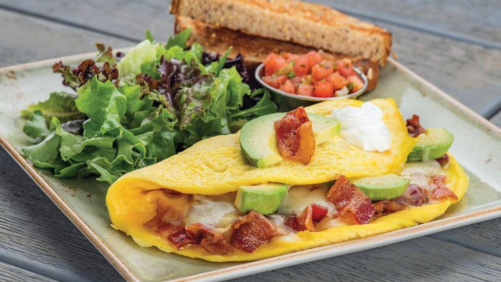 Bacado Omelet · Bacon, avocado, and Monterey Jack. Topped with sour cream and a side of housemade pico de gallo. Served with whole grain artisan toast with all-natural house preserves and lemon dressed organic mixed greens.