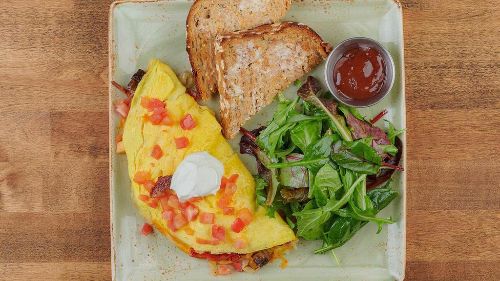 The Works Omelet · Ham, bacon, sausage, house-roasted crimini mushrooms, onions, and tomatoes with cheddar and Monterey Jack. Topped with all natural sour cream. Served with whole grain artisan toast with all-natural house preserves and lemon dressed organic mixed greens.
