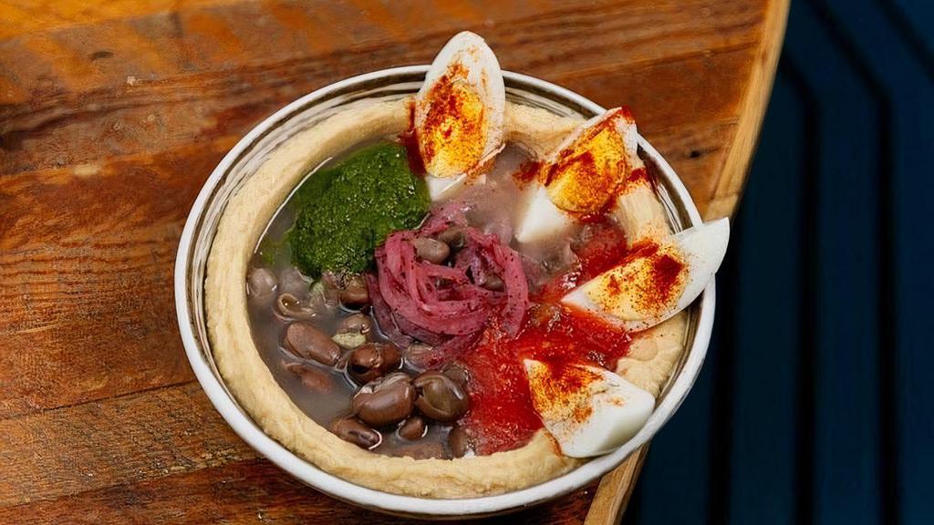 Hummus Ful · Hummus topped with tahini, stewed fava beans, grated tomato, green schug, sumac red onion and 1 hard boiled egg.  Served with 1 Pita.. *It's gluten-free when ordering gluten-free pita. *If sharing, recommended to add extra pita.