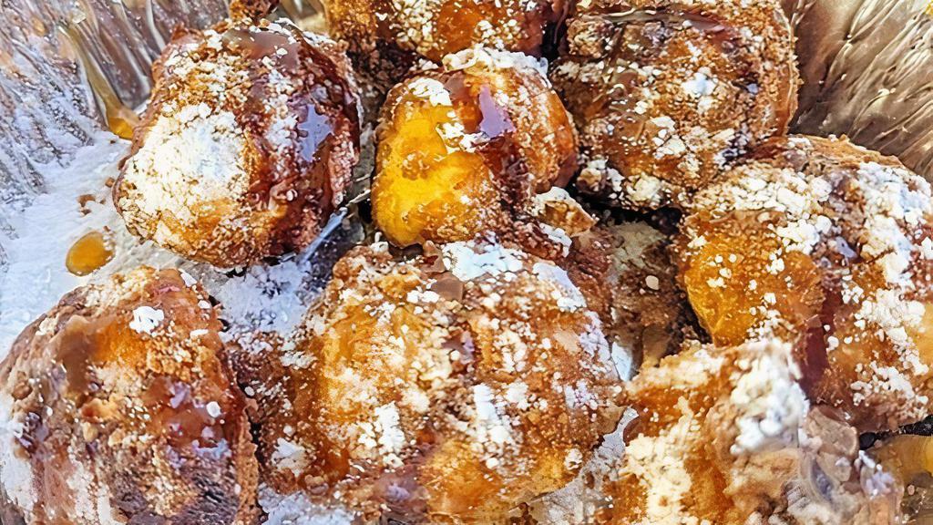 Cheesecake Bites · Deep-fried, battered Cheesecake balls, covered in powdered sugar, topped with chocolate and caramel syrup