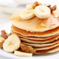 Golden Pancakes With Fresh Bananas · Fluffy golden pancakes topped with fresh bananas and served with a side of syrup and butter.