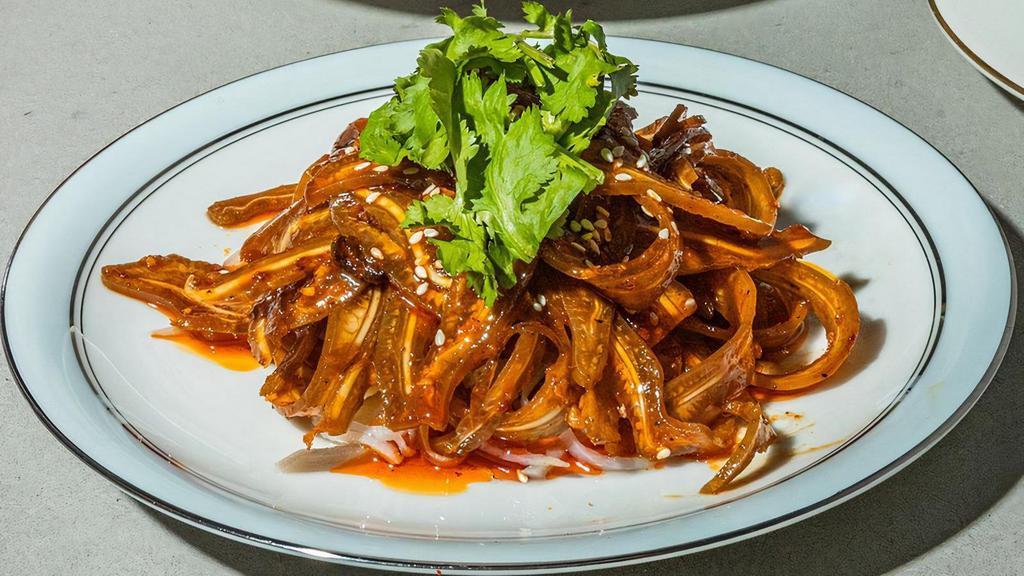 Pig Ear In Chili Oil · Thin, Tender Slices of Pig Ear Marinated in a Savory, Spicy, Numbing Sauce on a Bed of Thinly Shredded Potato. Garnished With Sesame Seeds and Cilantro. Served Chilled.