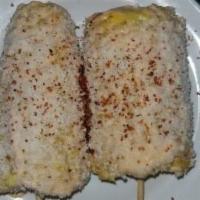 Elote · Roasted corn topped with chipotle mayo, cotilla cheese, chili pepper served on a cob.