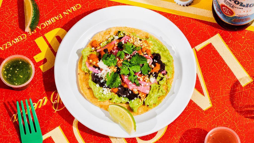 Avocado Tostada. · Guacamole, pickled red onion, queso fresco, cilantro and slightly spicy dried chile salsa over black bean spread on a crisped corn tortilla. Often described as “our most underrated menu item”!