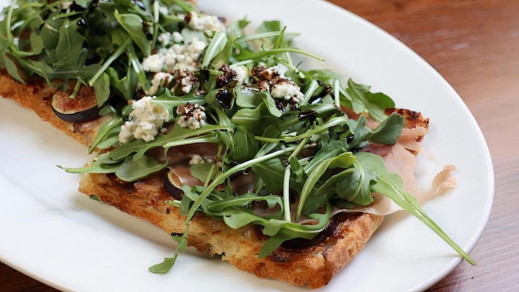 The Fig & Pig Flatbread · Crispy flatbread topped with blue cheese dressing, fresh figs, prosciutto, wild arugula, blue cheese crumbles and balsamic reduction.