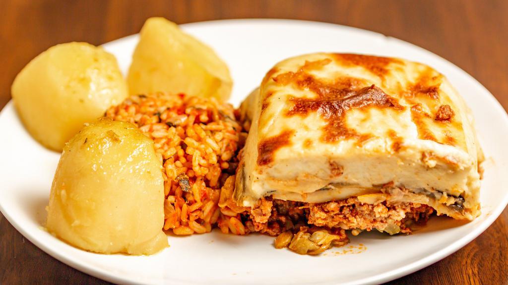 Moussaka · Casserole made by layering eggplant, potatoes and zucchini with a spiced meat filling, topped off with a creamy béchamel sauce that is baked to golden perfection served with lemon potatoes and spinach rice.