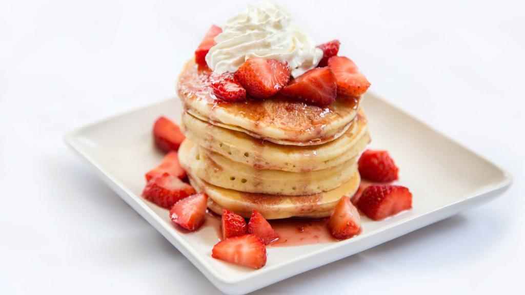 Strawberry Pancakes · A stack of 3 fluffy pancakes topped with locally grown sliced strawberries then dusted with powdered sugar and served with a side of butter and syrup.