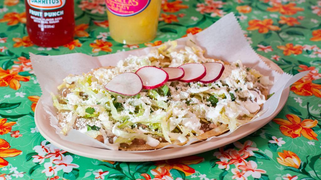 Huarache De Pollo Asado · Hand made flat corn tortilla served with grilled chicken, a layer of refried beans, lettuce, sour cream, queso Cotija, radish, cilantro and onions.