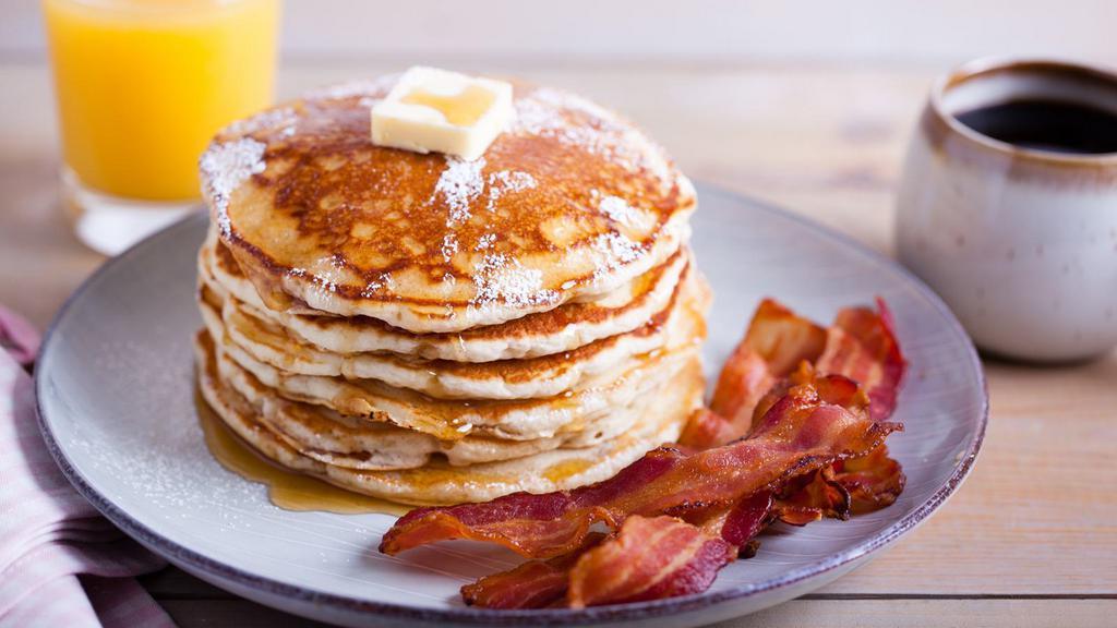 Bacon Buttermilk Pancakes · Three perfectly fluffy pancakes topped with crispy bacon served with a side of butter and syrup.