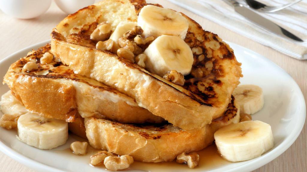 Banana French Toast · Sliced challah bread soaked in eggs and milk, then fried and topped with bananas served with a side of butter and syrup.