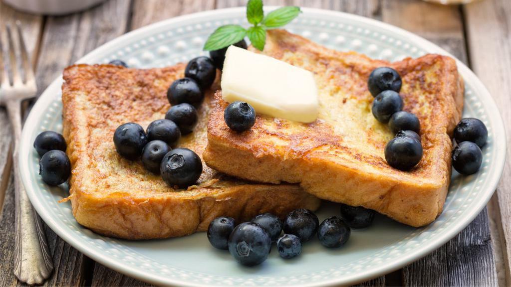 Blueberry French Toast · Sliced challah bread soaked in eggs and milk, then fried and topped with blueberries served with a side of butter and syrup.