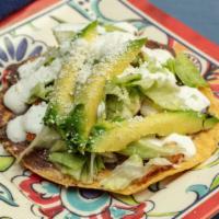 Tostada · Crispy corn tortilla topped with re-fried beans, lettuce, sour cream, avocado, and ground co...