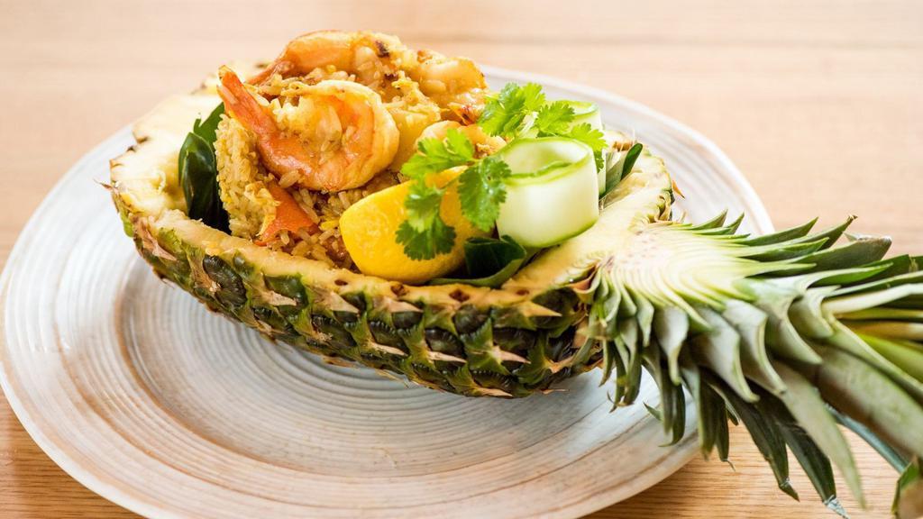 Pineapple Fried Rice · Jasmine rice stir fried with pineapple, onions, scallions, tomatoes, carrots, raisins, curry powder and egg. Garnished with roasted cashew nuts and cilantro.