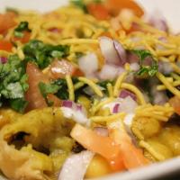 Samosa Chaat · Flattened samosas covered with chickpeas curry, chopped onions, tomatoes, coriander and chut...