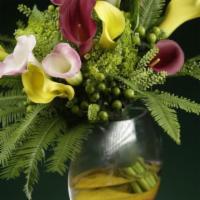 Callas Sunrise · Mix of Callas, green hydrangeas and berries, umbrella fern leaves in a designer’s clear vase...