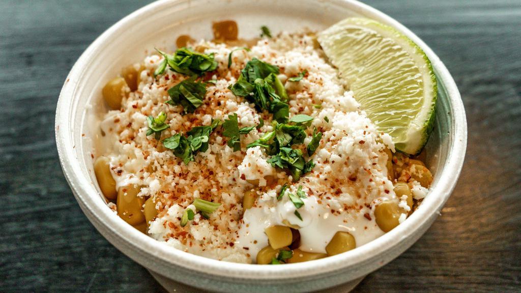 Esquites · Layers of corn, crema, & cotija cheese, topped with tajin, cilantro & a lime wedge in a cup.