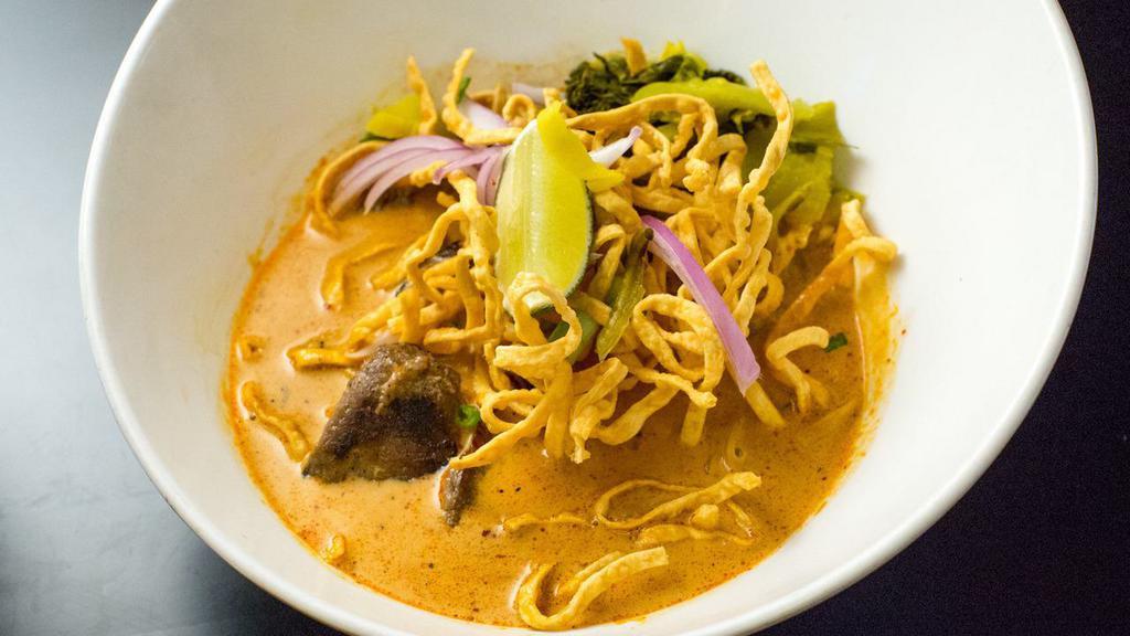Kow Soi (Curry Noodle Soup) · Hot. Spicy. Northern Thai style egg noodle in curry sauce with red onions, and dried shallots topped with crispy noodles and Thai pickle.