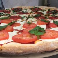 Caprese Pizza · Topped with classic cheese, pesto, tomatoes, red onions, and fresh basil.