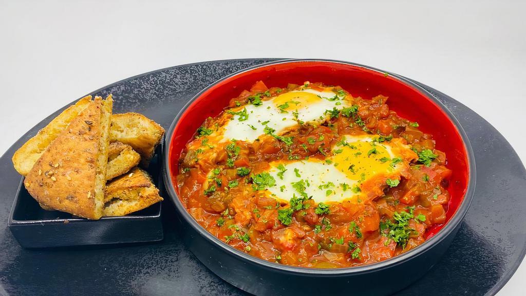 Shakshuka · Poached eggs cooked in a tomato and pepper sauce served with fresh pita, tahini, fresh cut vegetables, and olives.