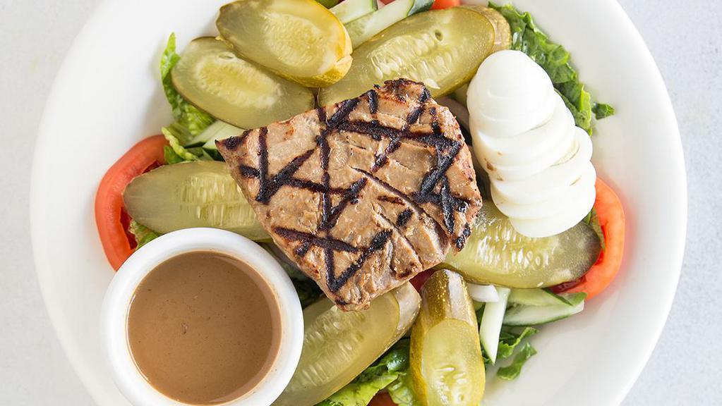 Tuna Nicoise Salad · Grilled tuna, olives, hard boiled eggs, tomatoes, and pickles served with vinaigrette on a bed of salad.