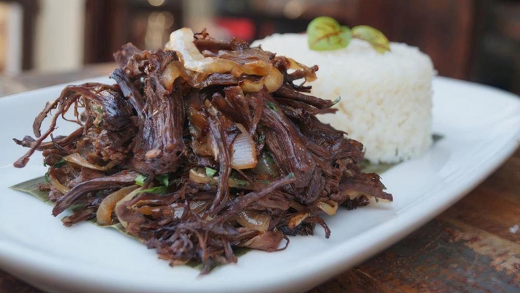 Vaca Frita · Pan - fried shredded skirt steak with garlic mojo, soy sauce, lime, onions, parsley, rice and beans