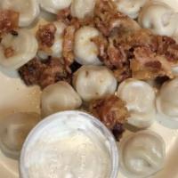 Koldunai · Meat dumplings topped with sautéed onions, bacon, and sour cream.