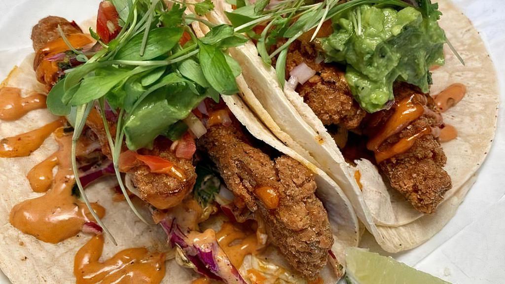 Baja Oyster Tacos · Loaded with fried Oyster mushrooms, crunchy cabbage slaw, guacamole and a creamy chipotle salsa. Topped with mico-cilantro and served with a fresh slice of lime. Gluten-Free!
