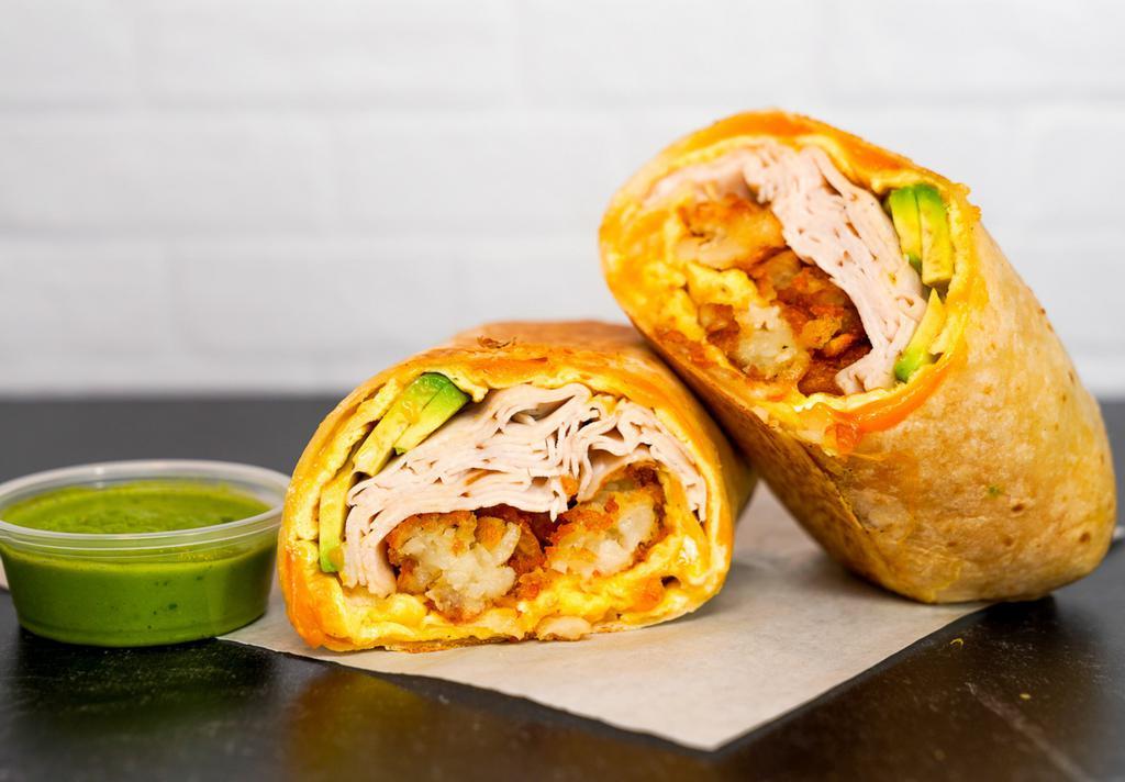 Smoked Turkey, Avocado, Egg, & Cheddar Breakfast Burrito · 3 fresh cracked, cage-free scrambled eggs, melted Cheddar cheese, sliced smoked deli turkey, fresh avocado, and crispy potato tots wrapped in a toasted 12” flour tortilla. Comes with avocado salsa verde side.