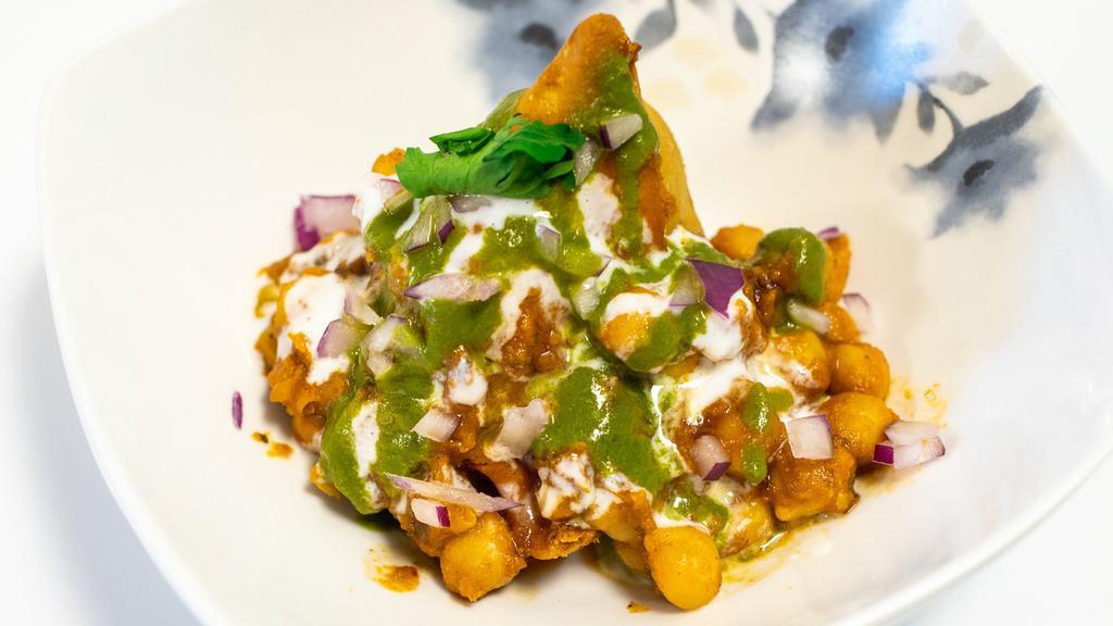 Samosa Chat · Crispy samosa served with chickpeas masala, yogurt, tamarind date, cool mind and coriander chutney. Topped with tomatoes, onions, cilantro, chickpea noodles and spice blend.