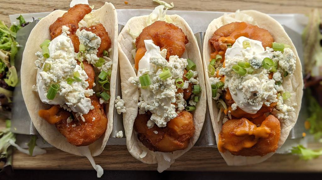 Buffalo Shrimp Tacos · Three crispy battered shrimp tacos drizzled in your choice of Buffalo sauce a top crisp cabbage and finished with a dollop of sour cream, green onion and bleu cheese crumbles.