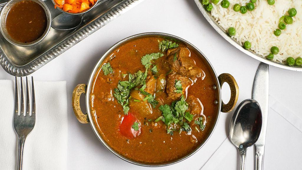 Lamb Korai · Lamb cubes curried in lightly spiced gravy with spring onion, tomato, green peppers, coriander leaf, and mild spices, served on a platter.