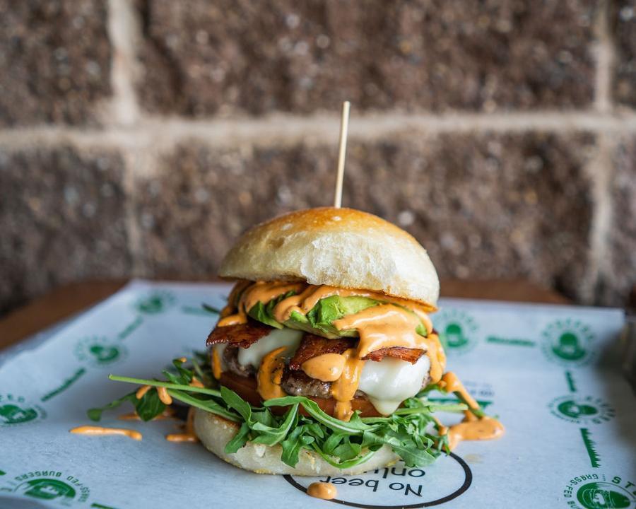 Avocado Blt Burger · Grass Fed Beef, topped with Swiss Cheese, Avocado, Applewood Smoked Bacon, Arugula, Tomato, and Chipotle Aioli served on a Country White Bun.