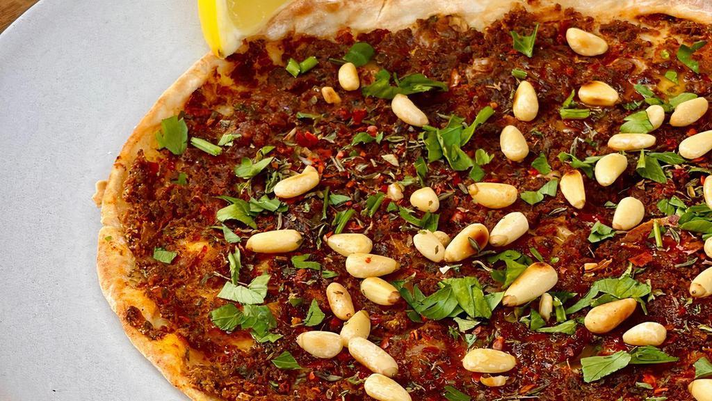 Lahm Bi Ajin · Traditional meat flatbread with pine nuts, house-made herby harissa and pomegranate vinaigrette. Contains nuts.