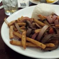 Lomo Saltado · Beef strips whit sautéed onions and tomatoes served whit french fries and white rice.