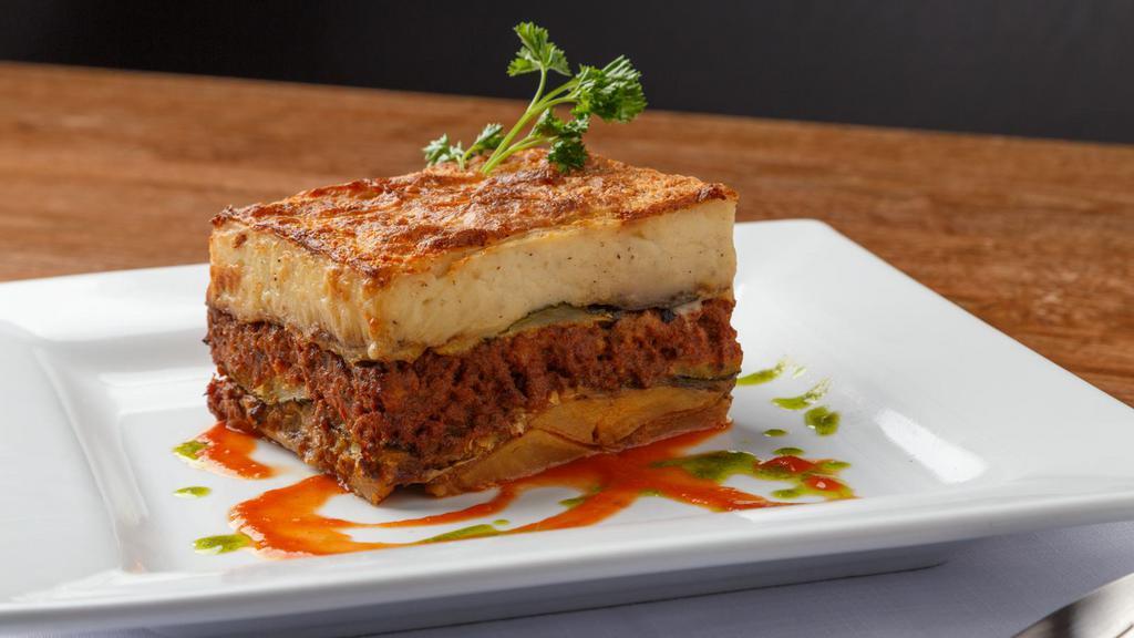 Seafood Moussaka · Gluten-free. Finely chopped seafood specialties in layers of zucchini, eggplant & yellow squash seared in EVOO, feta béchamel sauce.