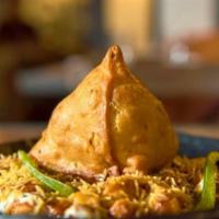 Samosa Chaat · A samosa with chickpeas, mint, tamarind, yogurt sauces, topped with chaat masala and cilantro.