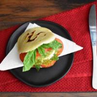 Capresa Arepa (V) · Grilled corn dough patty filled with mozzarella cheese, sliced tomatoes, fresh basil, and pe...