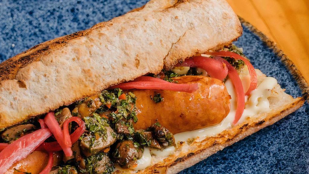 Choripan · Portuguese linguica sausage, roasted mushroom chimichurri, pickles red onion, roasted garlic aioli, French baguette.