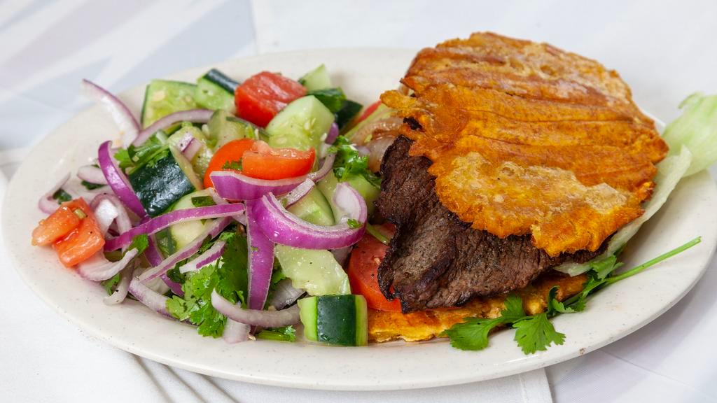 Platano Sandwich De Bistec · Grilled Steak On A Fried flattened green plantains instead of bread Topped Lettuce Tomatoes.