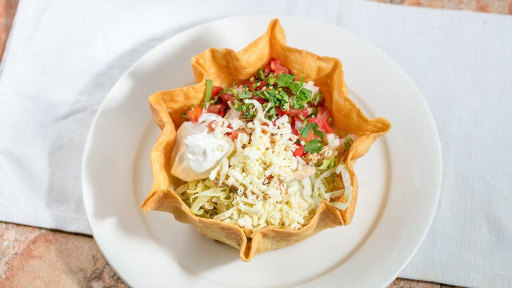 Taco Salad · Fried tortilla shell filled with ground beef or shredded chicken, beans and cheese sauce, topped with lettuce, tomatoes, guacamole sour cream and shredded cheese.